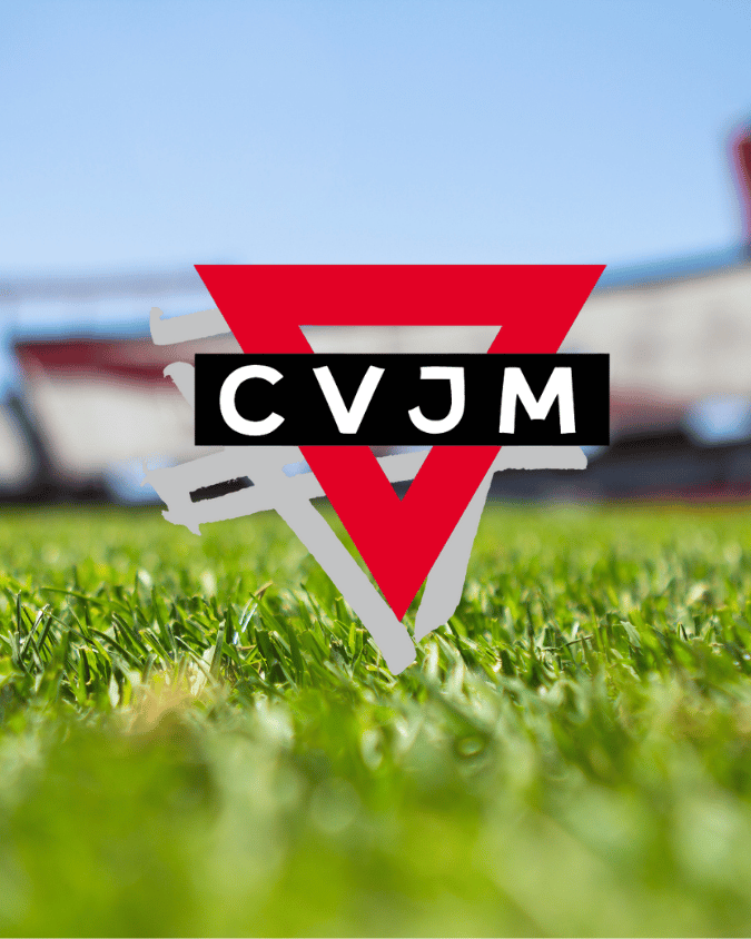 Das Logo der CVJM mit einem verschwommenem Hintergrund von einem Rasen und blauen Himmel.